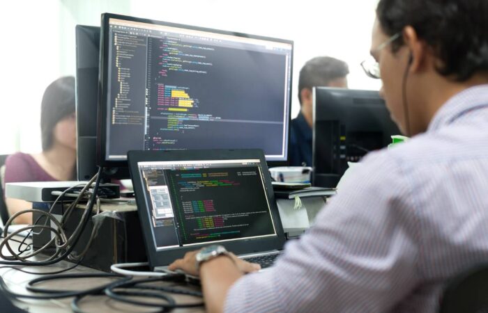 Photo of man at a laptop and computer desk, writing lines of code