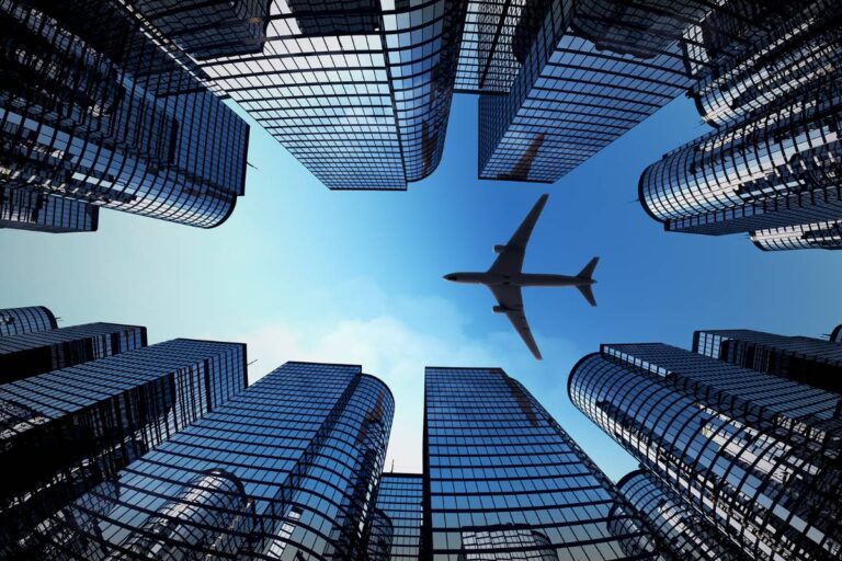 Photo looking up through a line of skyscrapers to view an airplane flying overhead