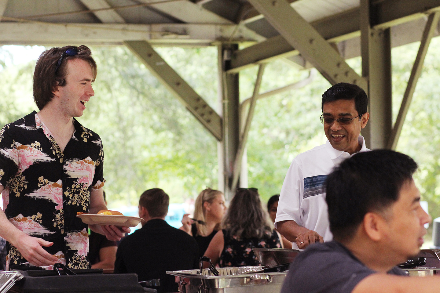 Chandan Mukhopadhyay (Synergy EVP & CTO) laughing and talking with another Synergist at company picnic while serving themselves food
